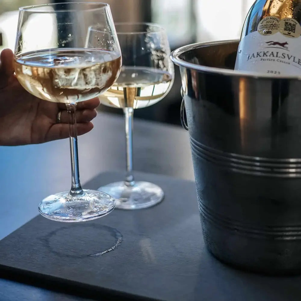 Two wine glasses with white wine, one being held, next to a bottle of wine in an ice bucket on a table.