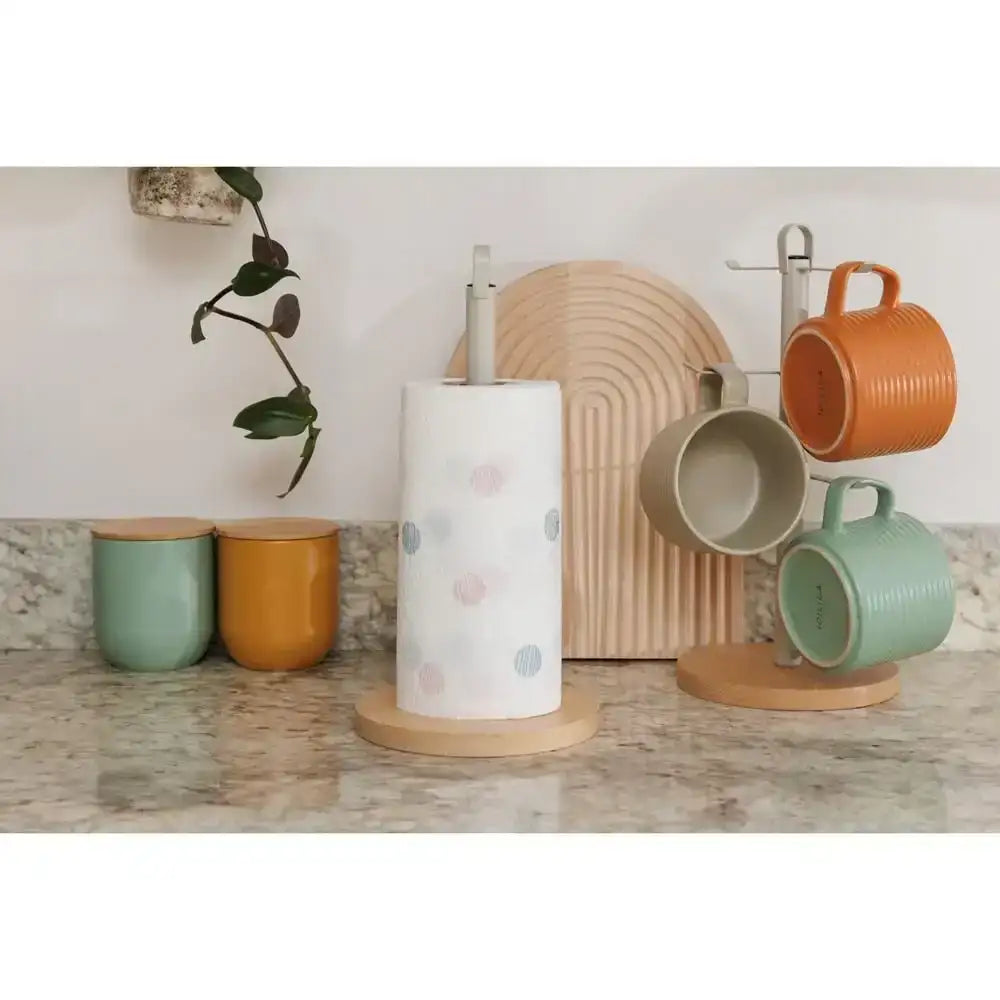 Colorful mugs on a stand with a paper towel holder on a kitchen counter.