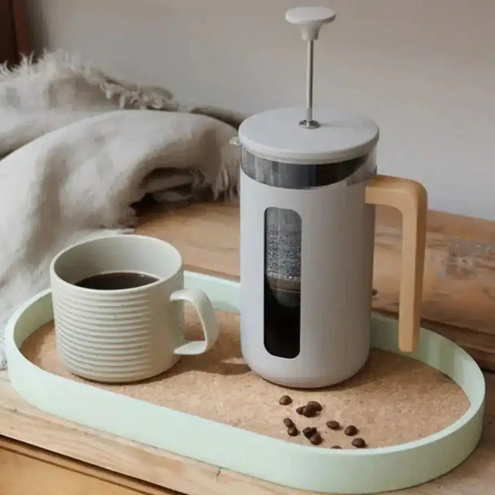 White French press coffee maker with a wooden handle on a tray next to a white mug filled with coffee.