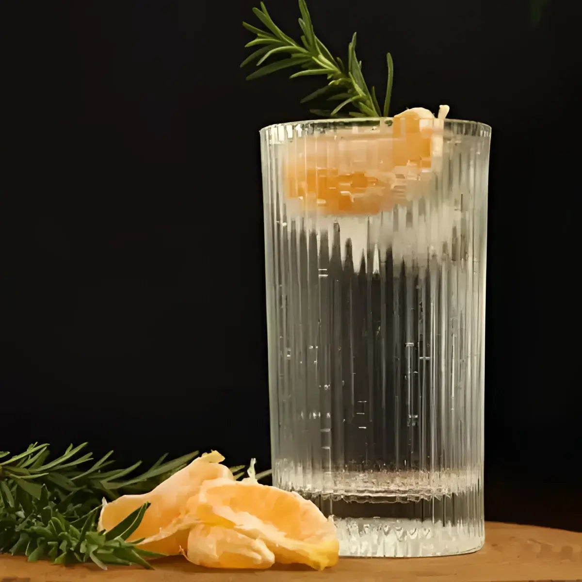Clear glass with a cocktail garnished with an orange peel and rosemary on a dark background