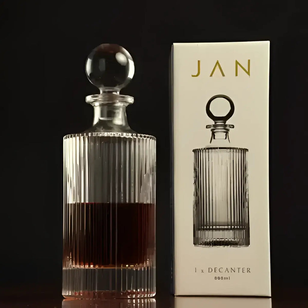 Glass decanter with dark liquid next to its packaging box on a black background