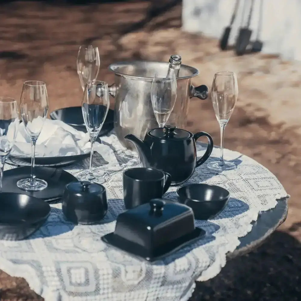 Black dinner set with champagne glasses on a patterned tablecloth outdoors