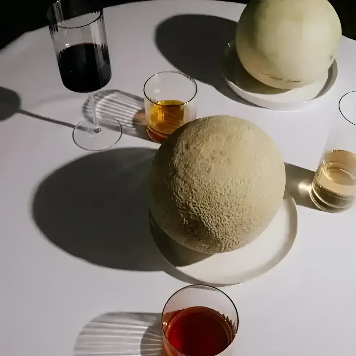 Two cantaloupes on a white tablecloth with glasses of red and white wine.