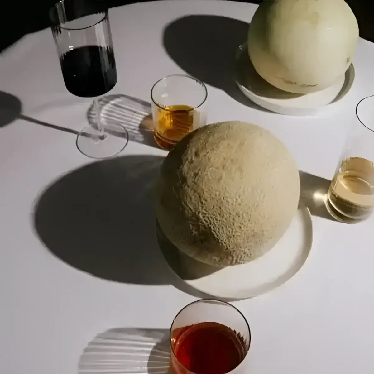 Two cantaloupes on a white table with glasses of red and white wine.