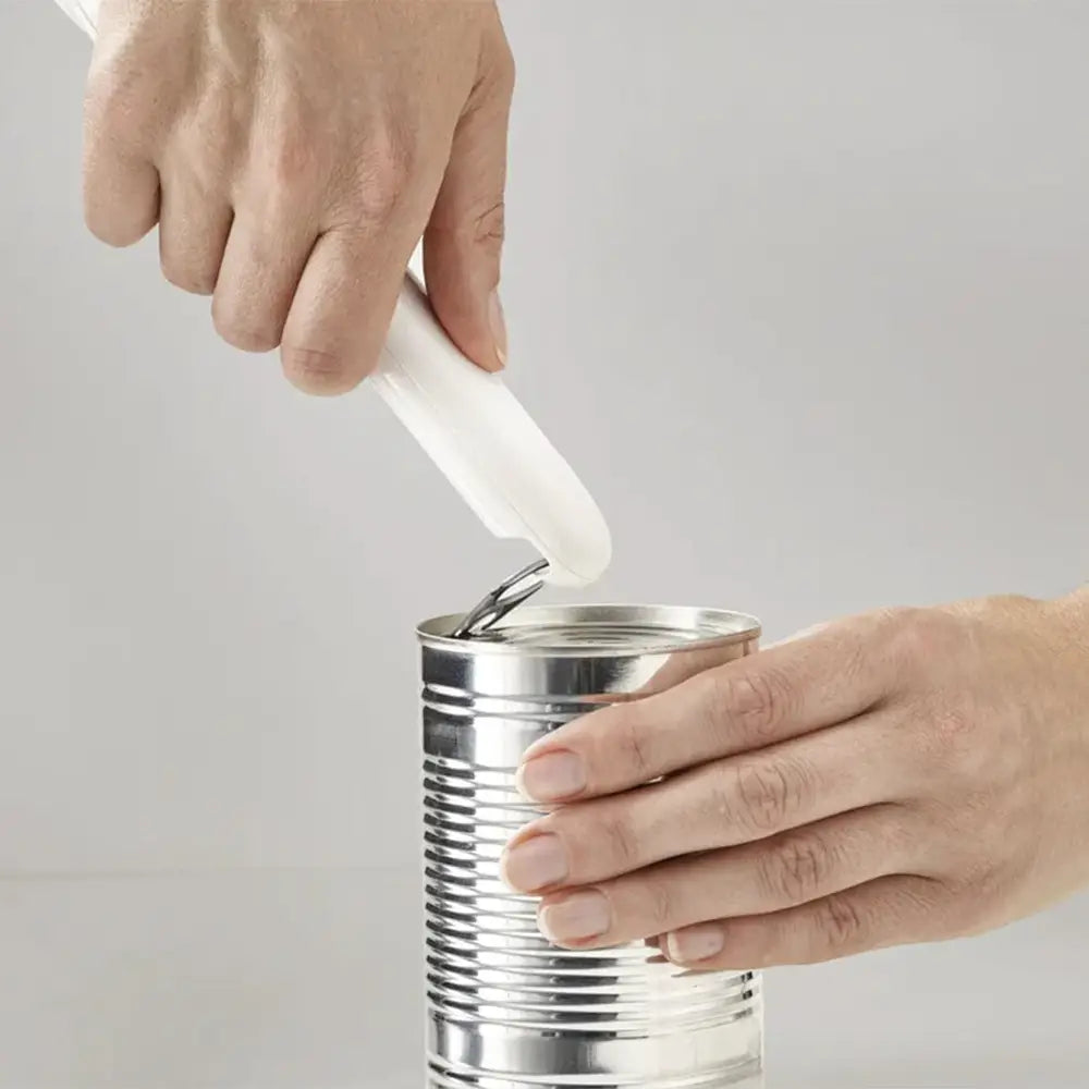 Hand using a can opener on a metal can against a plain background