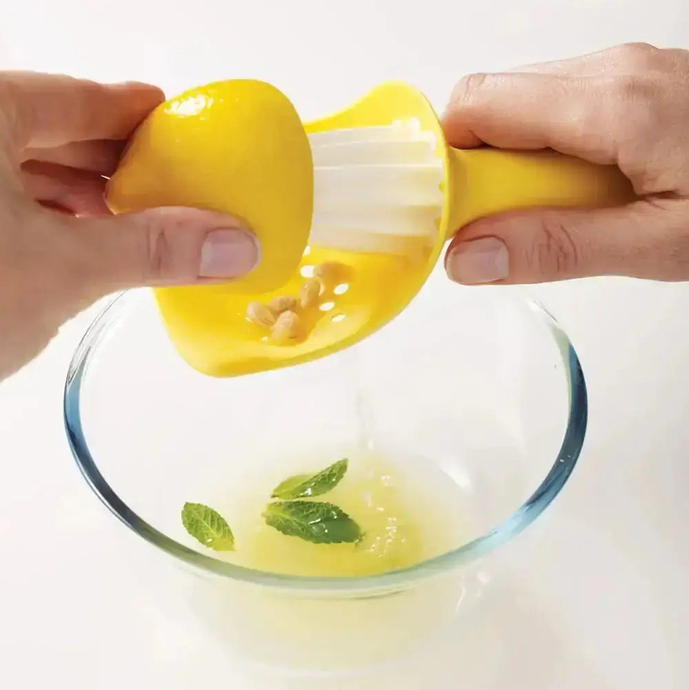 Yellow citrus juicer being used to extract juice from a lemon over a glass bowl with mint leaves.