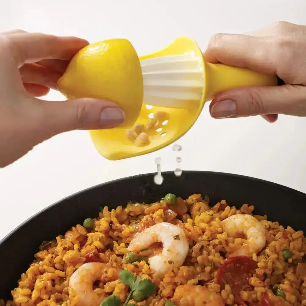 Person squeezing a lemon over a dish of paella with shrimp and peas.