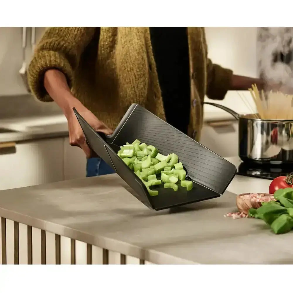 Person holding a black kitchen scoop filled with chopped celery in a kitchen setting.