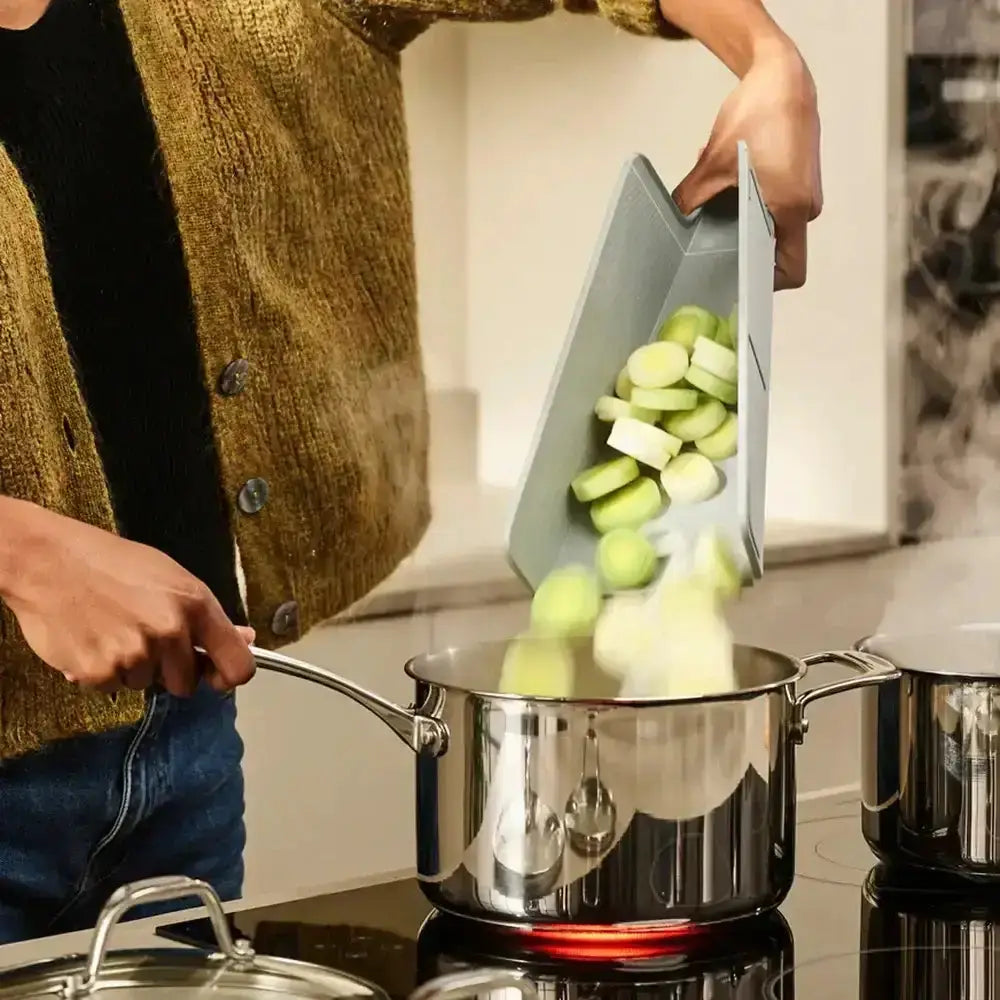 Person cooking with a pot on a stove, using a knife to add ingredients.