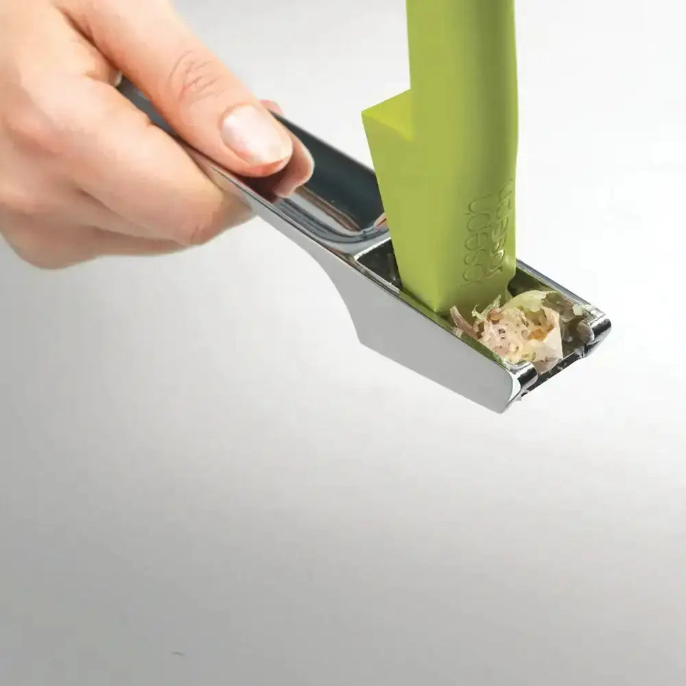 Hand using a green kitchen tool to extract seeds from a fruit on a gray background
