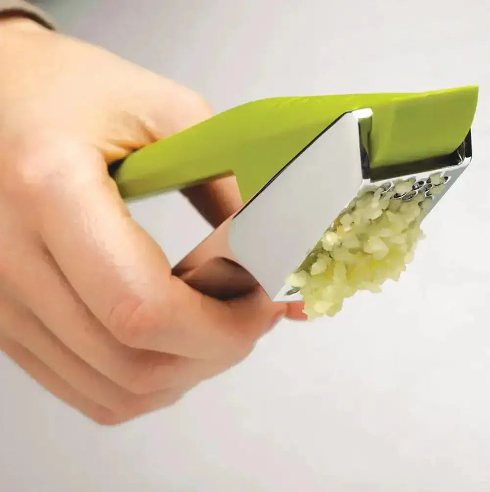Hand holding a garlic press with minced garlic on a white background