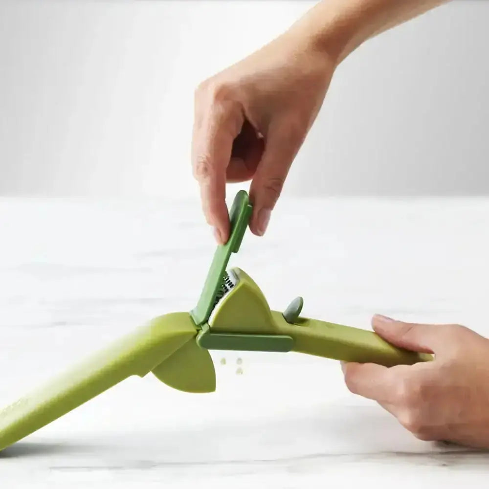 Green kitchen tool being used to grate a vegetable on a white background