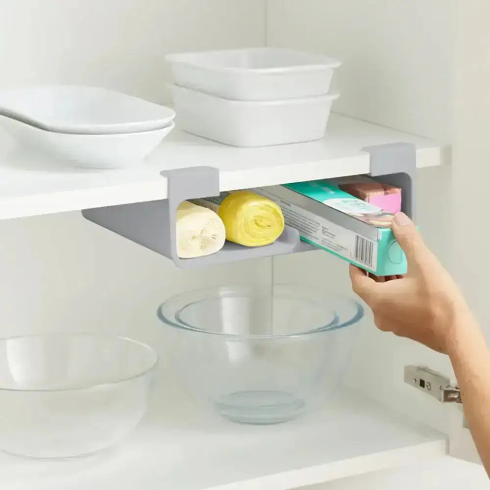Hand using a small gray shelf to store items under a kitchen counter.