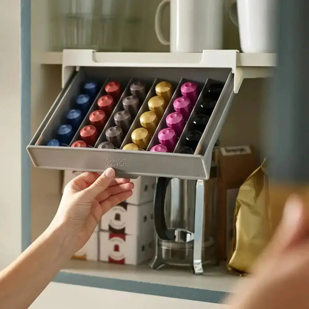 Hand opening a drawer filled with colorful coffee pods in a kitchen setting.