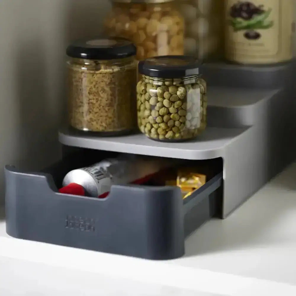 Gray kitchen shelf with jars and a drawer containing food items on a white surface.