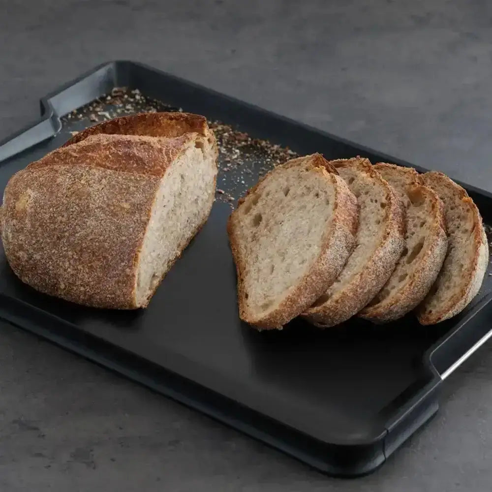 Loaf of bread with slices on a black tray against a dark background