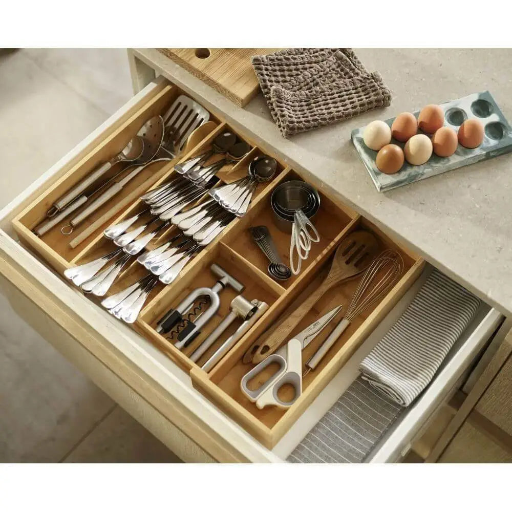 Open kitchen drawer with organized utensils and a cutting board on a countertop.