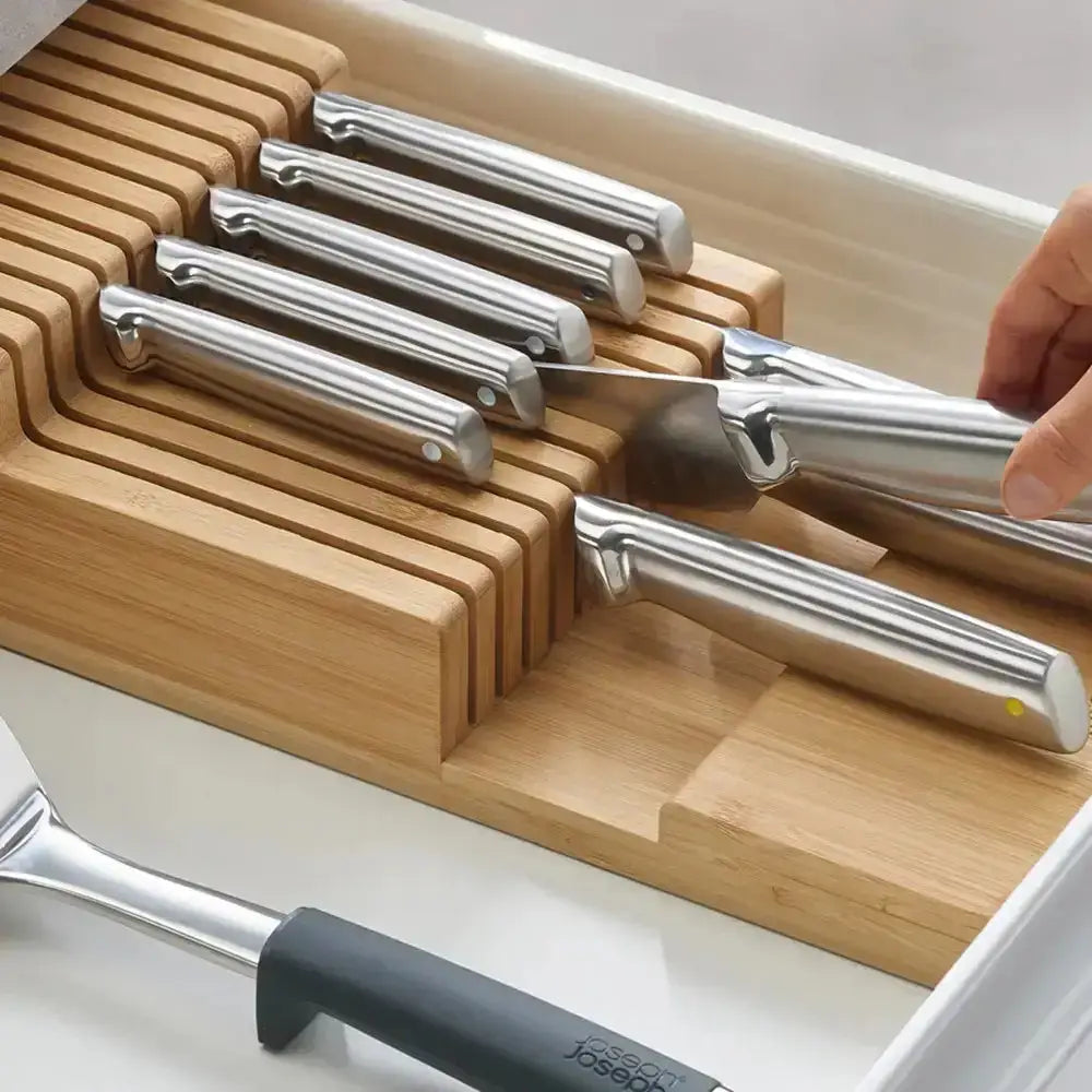 Wooden knife block with silver knives and a hand reaching for one, set against a white background.