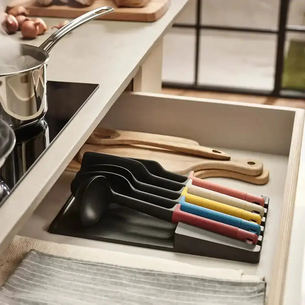 Set of colorful ladles in a kitchen drawer with wooden utensils.