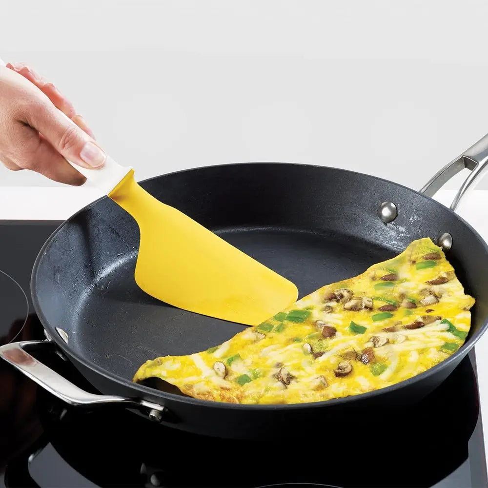 Person using a yellow spatula to flip an omelette in a black frying pan on a stove.