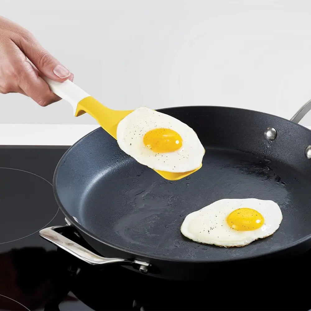 Person using a yellow spatula to flip an egg on a frying pan.
