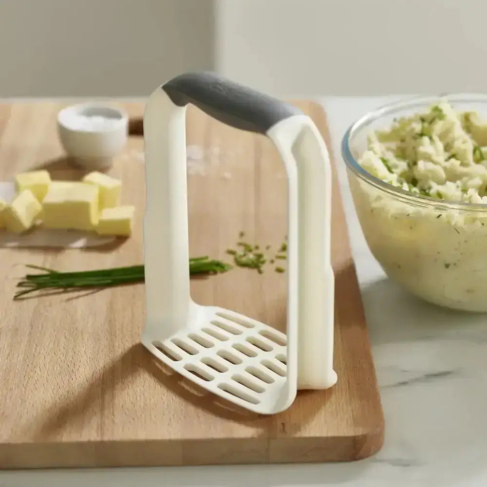 White kitchen tool on a wooden cutting board with ingredients in the background