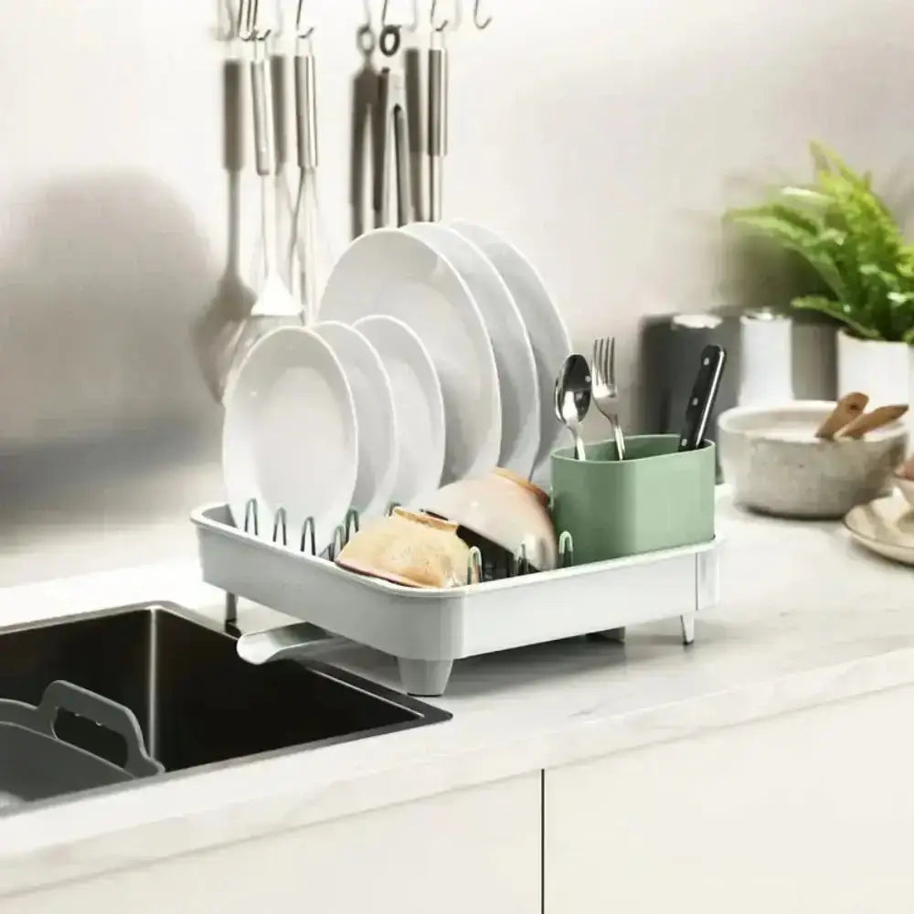 Dish drying rack with plates, bowls, and utensils on a kitchen counter.