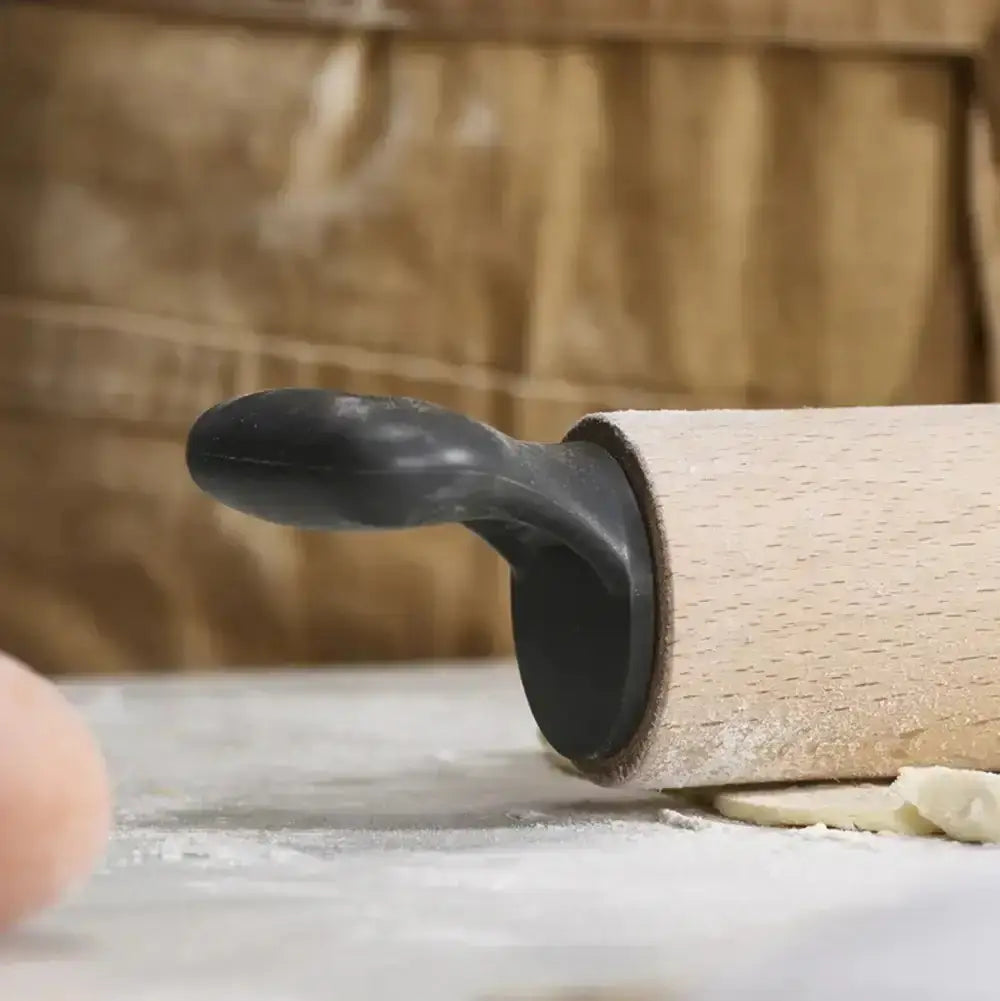 Wooden rolling pin with a black handle on a wooden surface with flour.