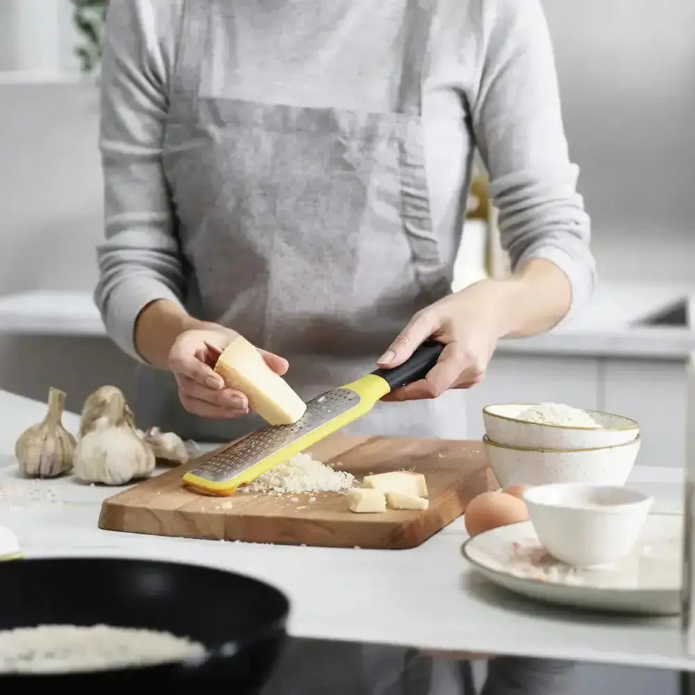 Person grating cheese on a wooden board with kitchen items around