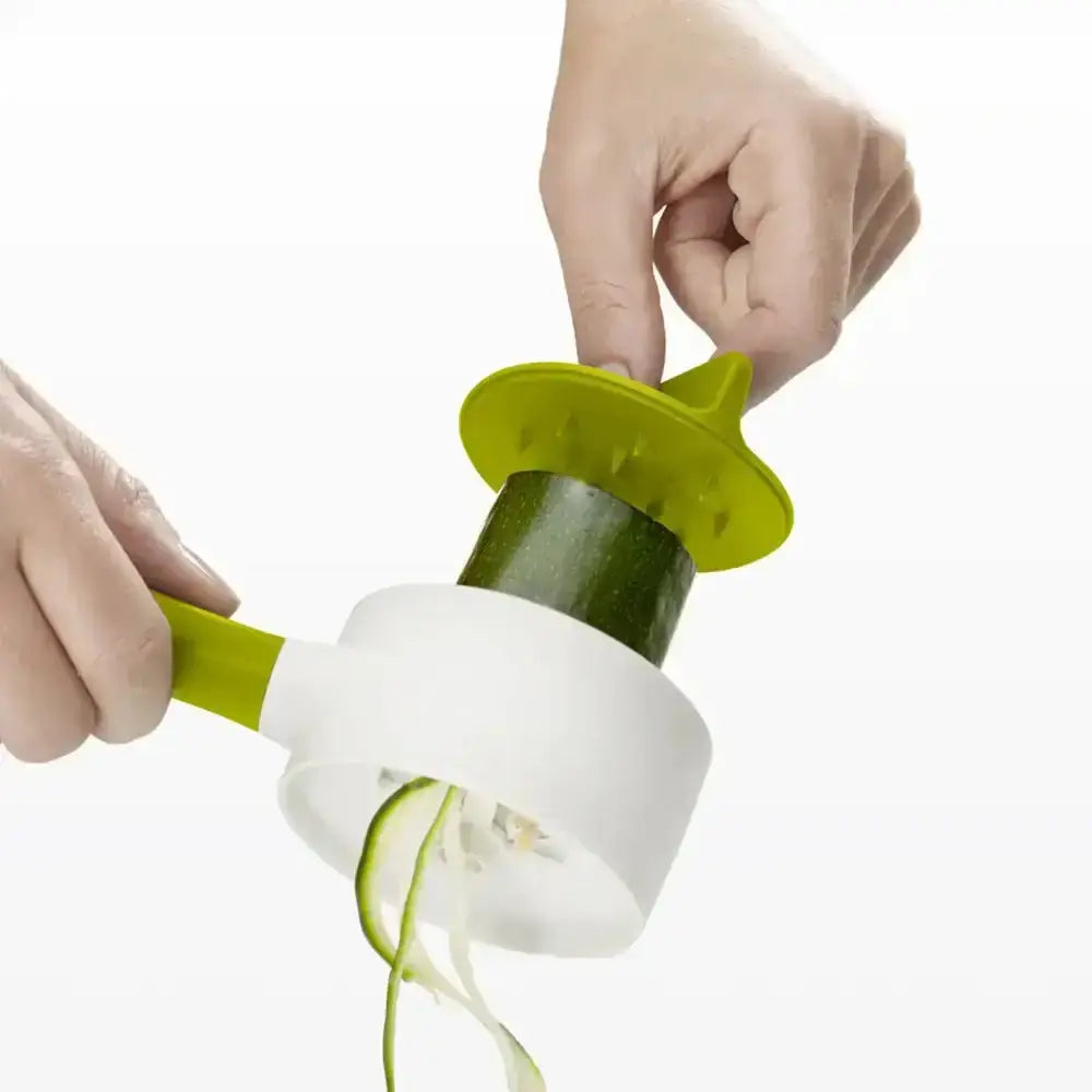 Hand using a green and white spiralizer to slice a zucchini on a white background