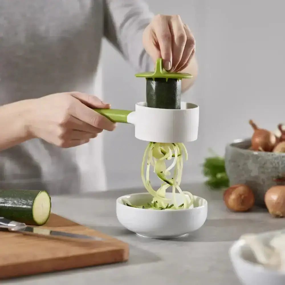 Person using a spiralizer to make zucchini noodles on a kitchen counter.