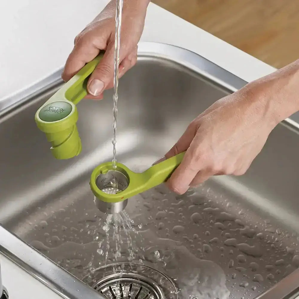 Person washing a green kitchen tool under running water in a sink.