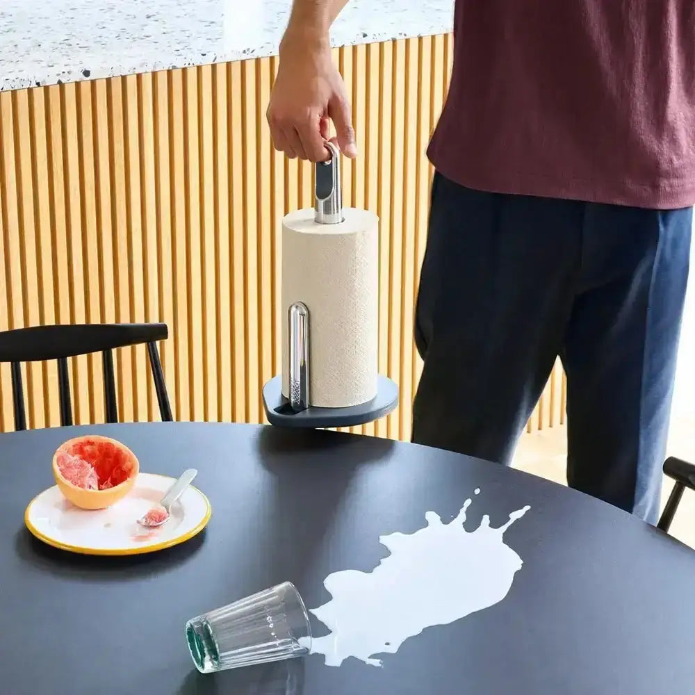 Person using a paper towel holder on a table with a glass and plate in the background