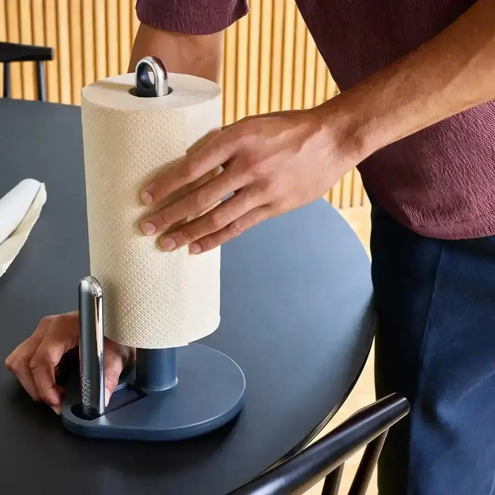Person using a paper towel roll on a blue stand at a table.