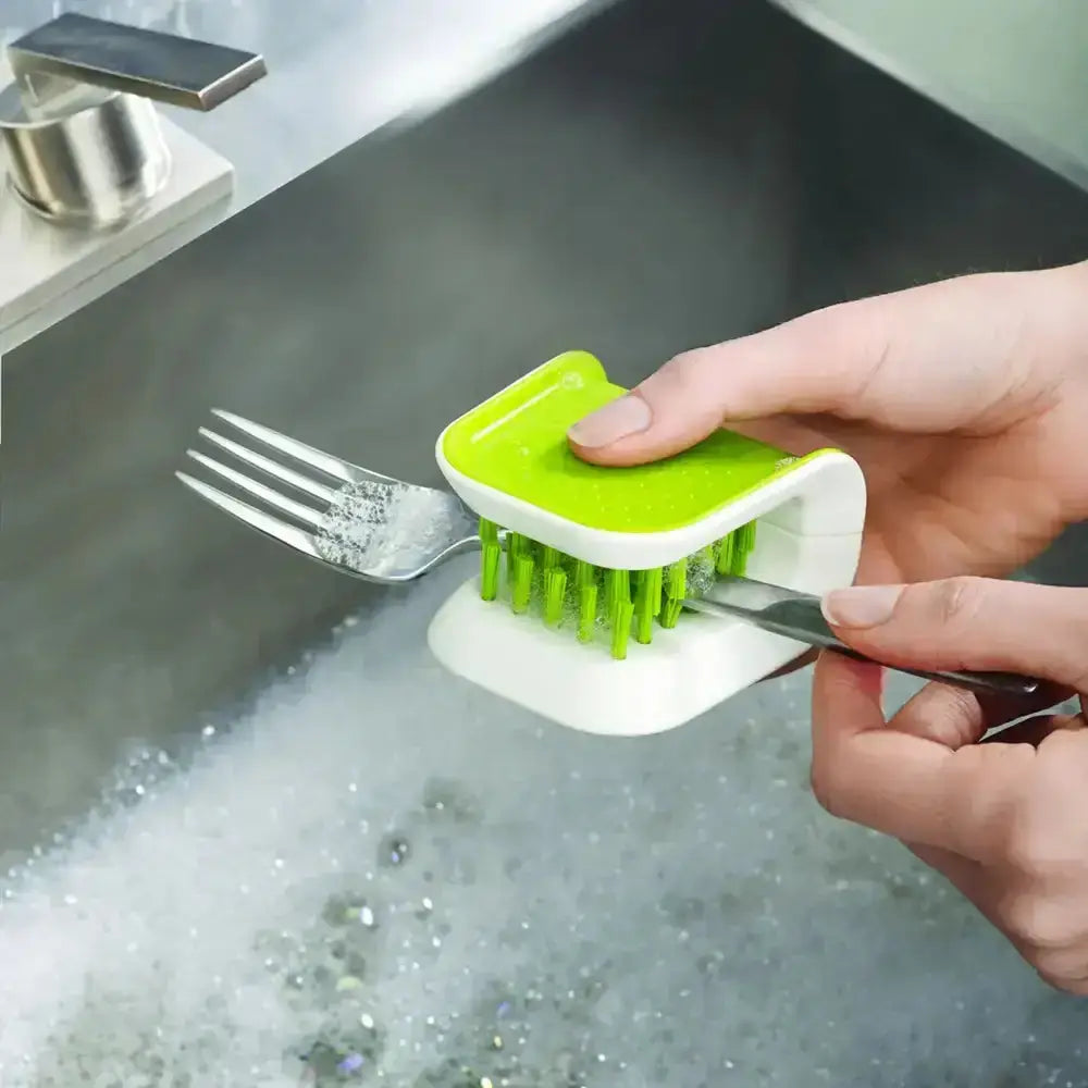 Person using a green and white dish scrubber to clean a fork in a sink.