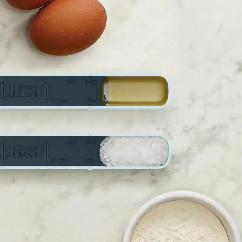 Two measuring spoons with spices on a marble surface with eggs and flour.