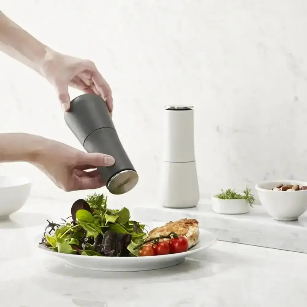 Person using a pepper grinder on a plate of salad with a white background