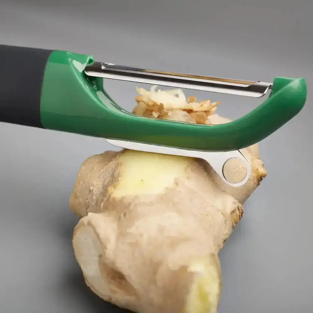 Green and black vegetable peeler on a ginger root against a gray background