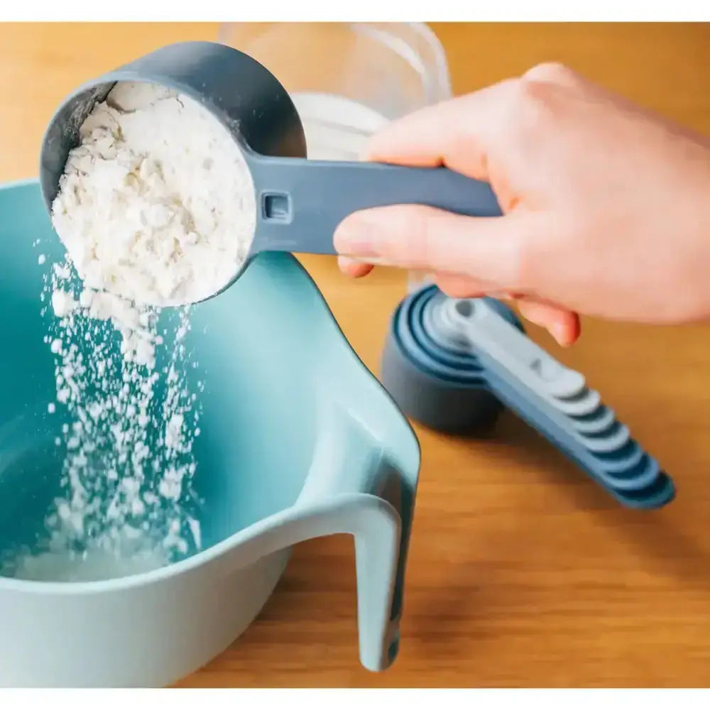 Hand using a measuring cup to pour flour into a bowl on a wooden surface