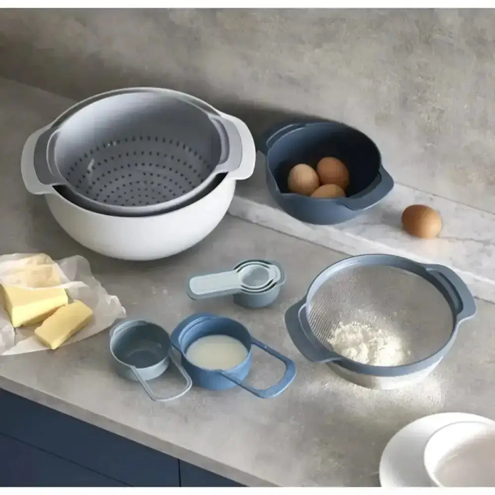 Set of kitchen utensils including a colander, bowls, and measuring cups on a gray countertop.