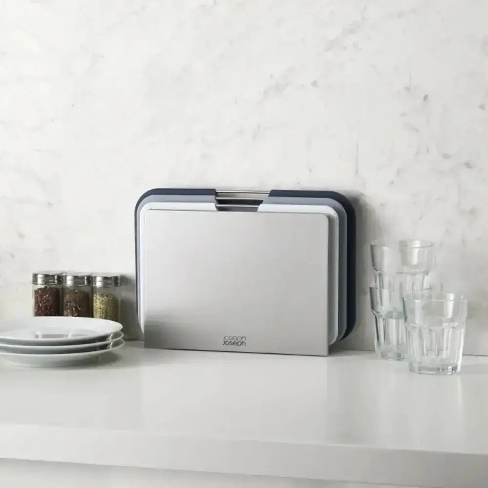 Kitchen countertop with a cutting board, glasses, and plates against a white marble wall.