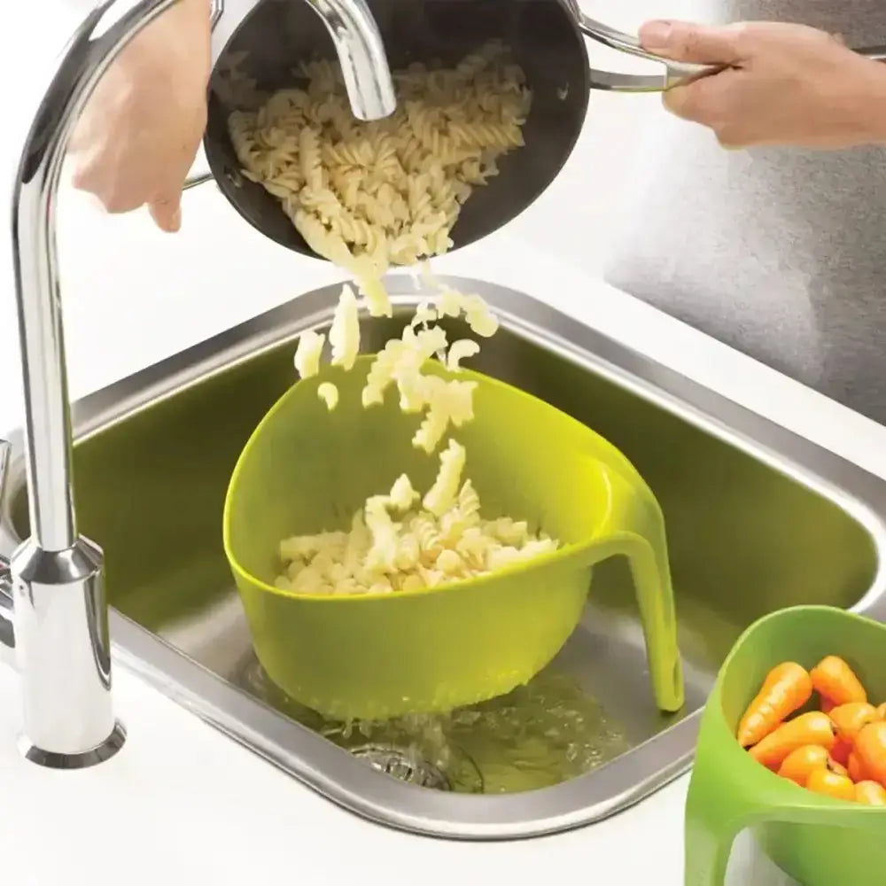 Pasta being drained into a green colander over a sink.