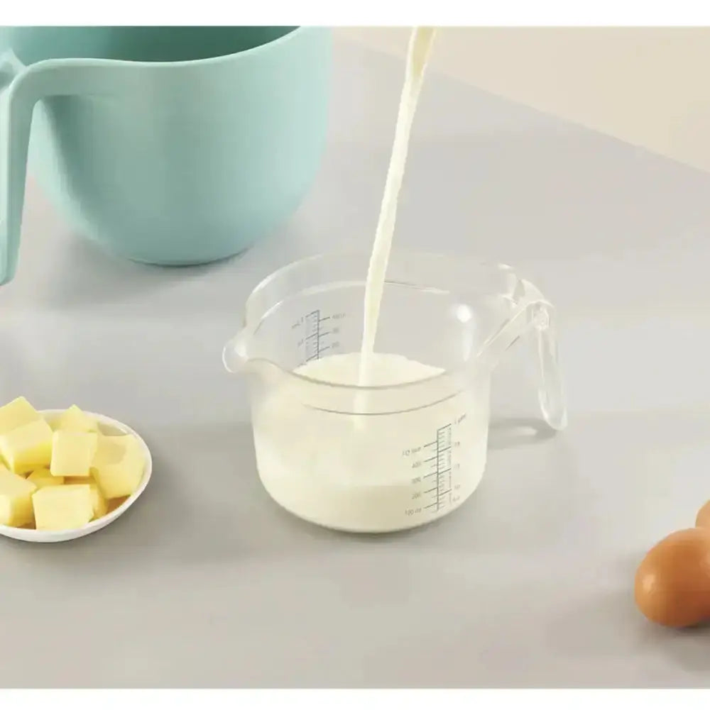 Measuring cup being filled with milk on a kitchen counter with butter and eggs.
