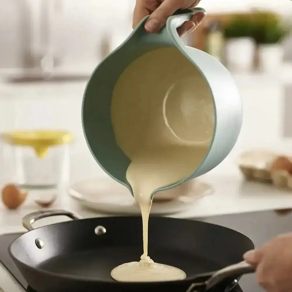 Person pouring batter from a green measuring cup into a black frying pan on a kitchen counter.