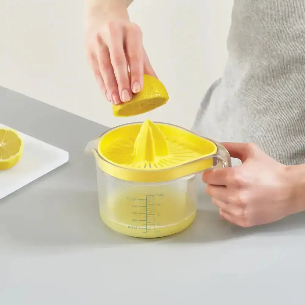 Person using a yellow lemon squeezer to extract juice from a lemon on a light gray surface.