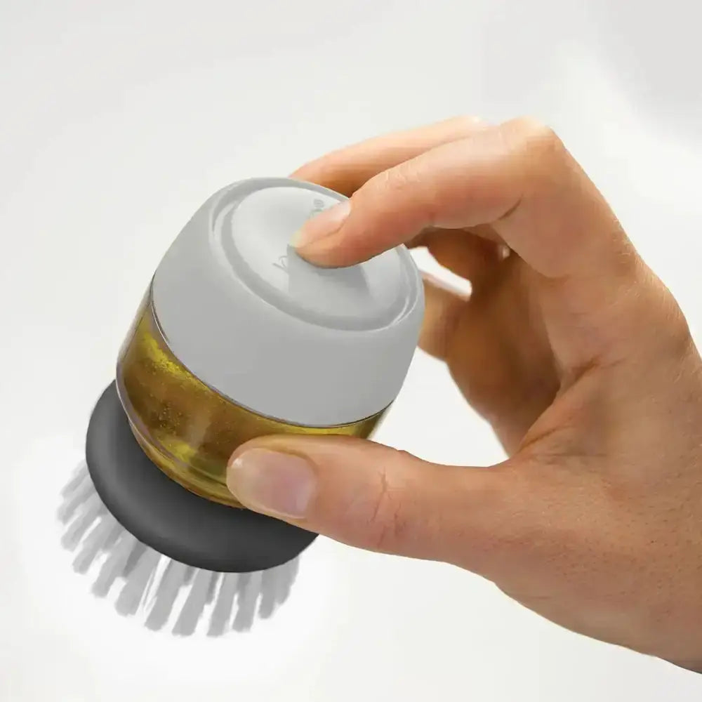Hand holding a kitchen brush with a container of oil on a white background