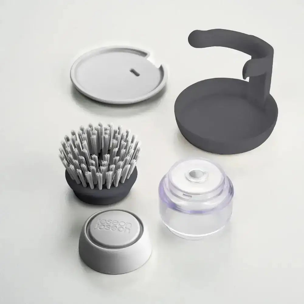 Set of kitchen cleaning tools including a brush, lid, and other components on a light background