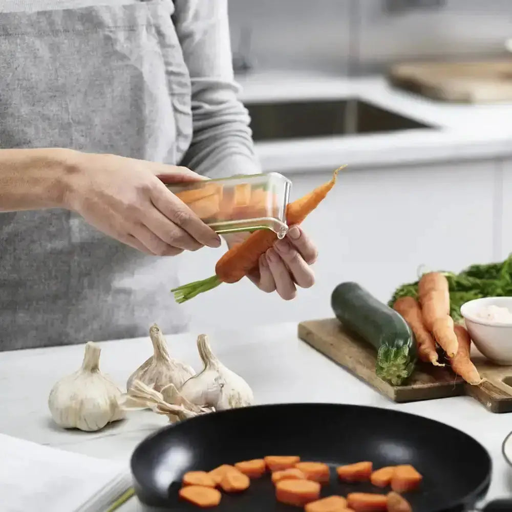 Person preparing vegetables on a kitchen counter with a pan of carrots.