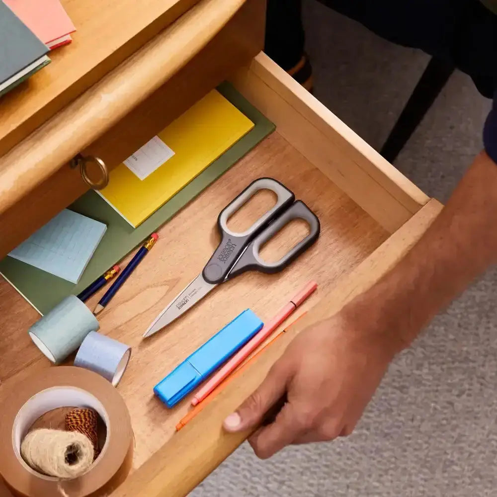 Open wooden drawer with stationery items including scissors, pens, and tape.