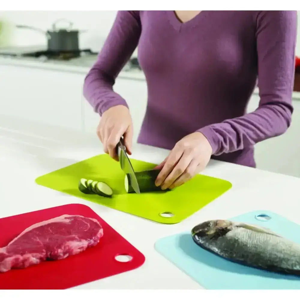Person cutting vegetables on a green cutting board with red and blue boards in the foreground